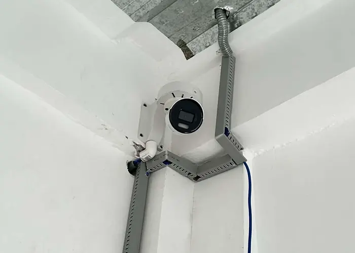 A CCTV camera mounted at a ceiling corner with the cable neatly coiled and secured below.