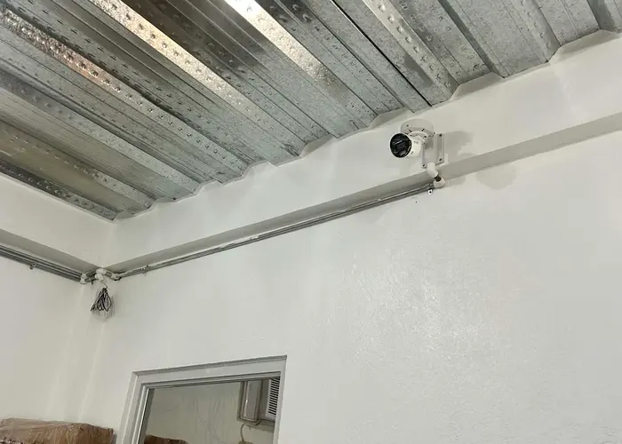 A Hikvision CCTV camera mounted at a ceiling corner, cable routed neatly through steel roof decking.