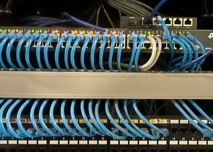 A network switch and patch panel with dozens of blue Cat6 cables neatly dressed and connected.