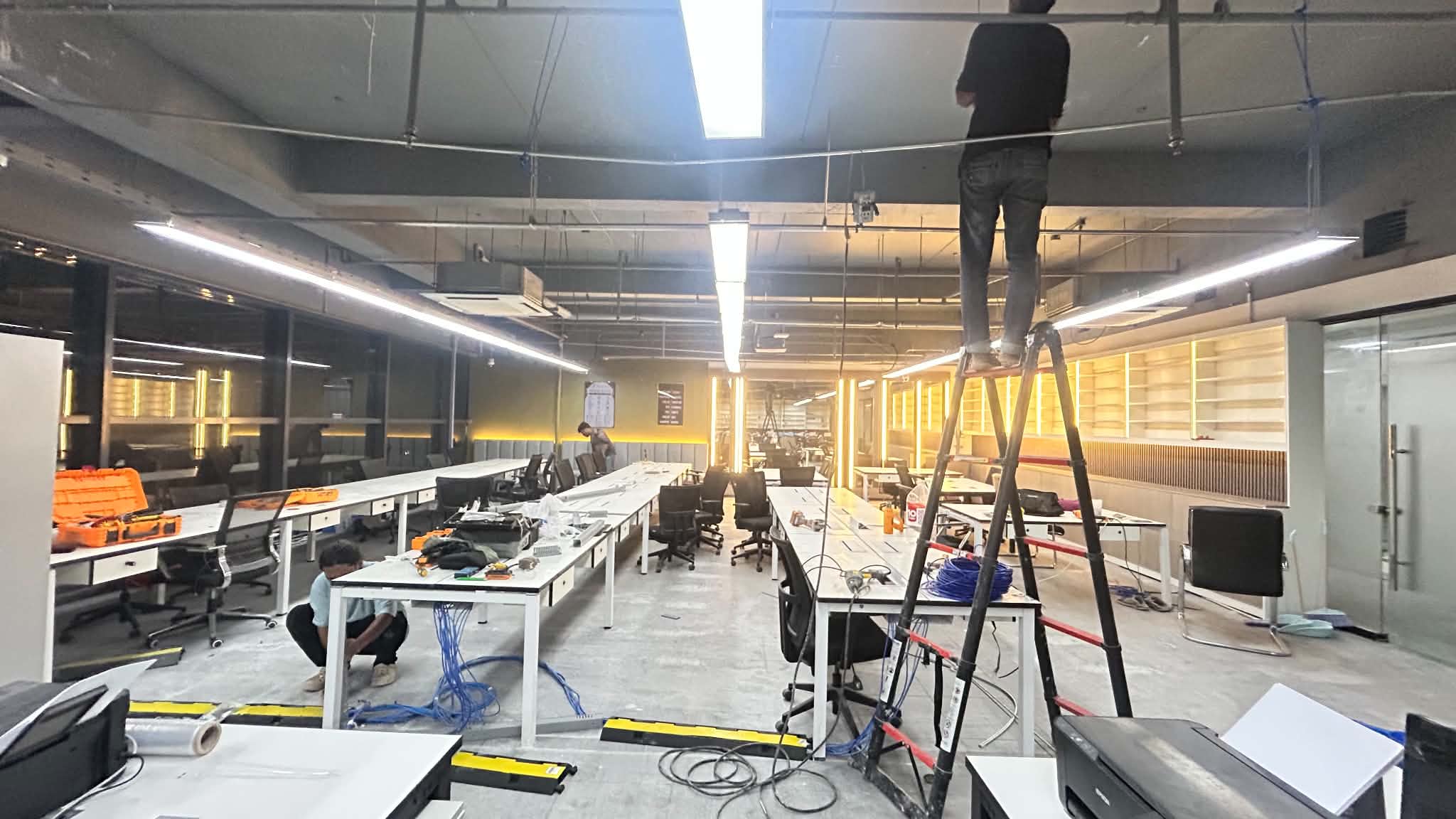 Open office workspace with tools, ladders, and ceiling work in progress.