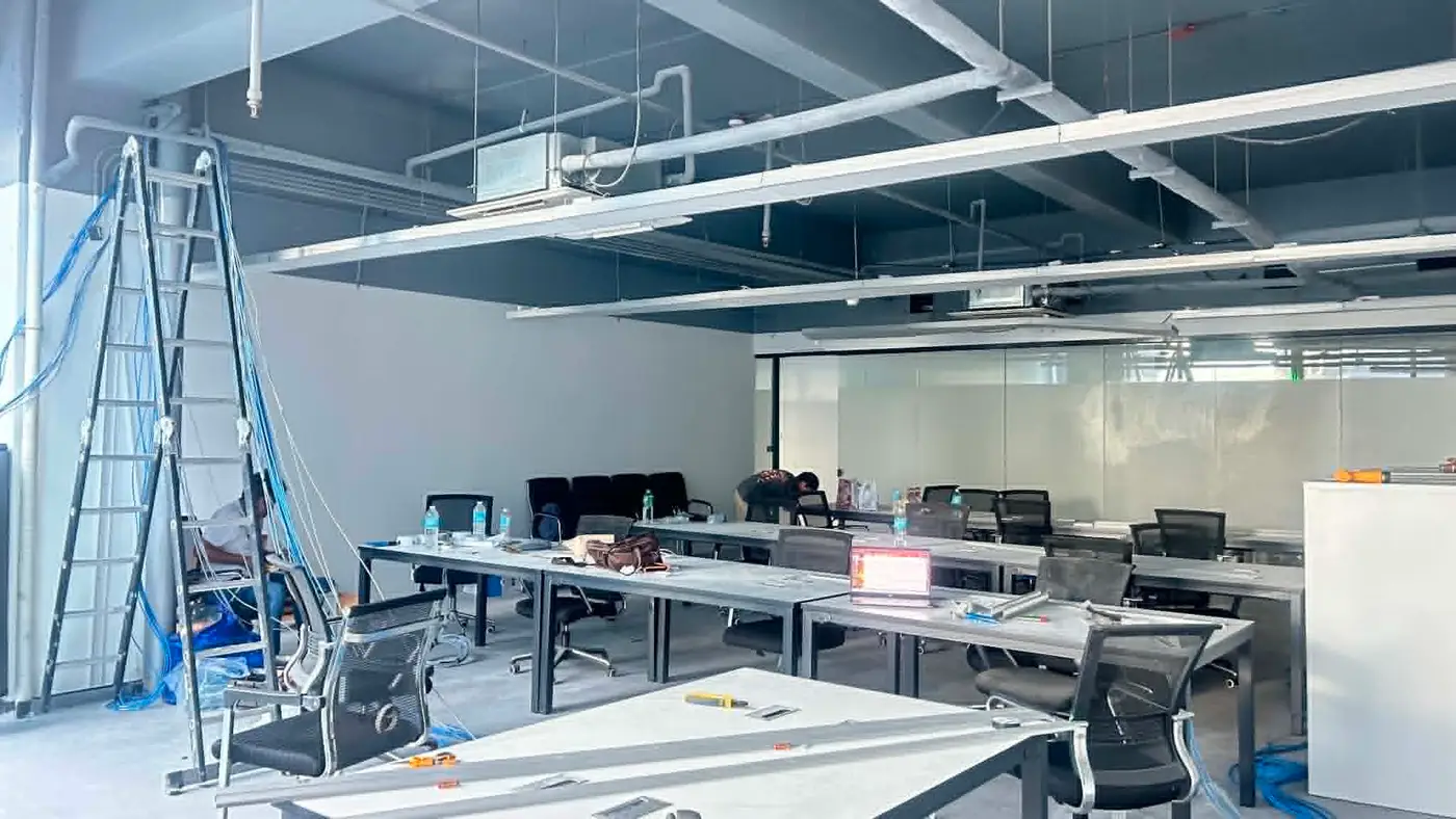 Open-plan office with newly installed ceiling cable trays above rows of desks.