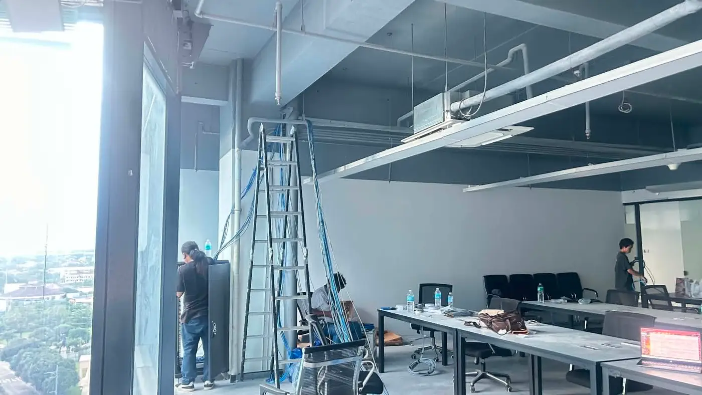 Technicians running structured cabling across an open office floor with the Mactan Newtown skyline visible through floor-to-ceiling windows.