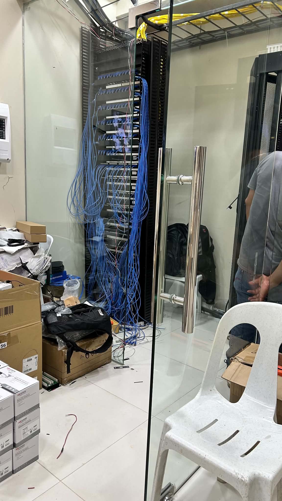 Open, unpopulated server rack frame in a glass-walled server room with bundles of blue Cat6 cable drops hanging down, ready for termination.