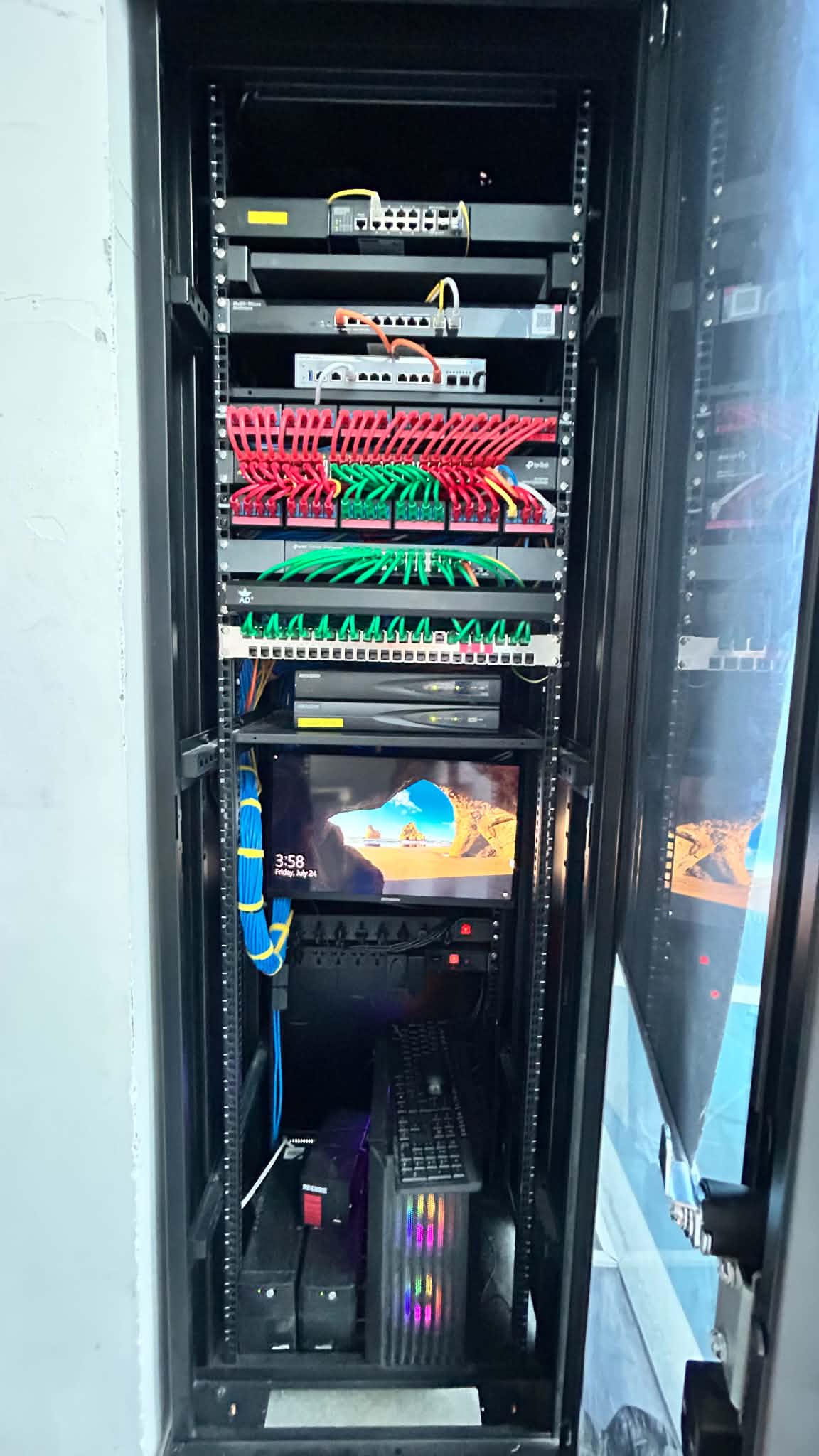Fully populated server rack with switches, color-coded red and green patch panels, a rack-mounted monitor and keyboard, dual NVRs, and a UPS at the base.