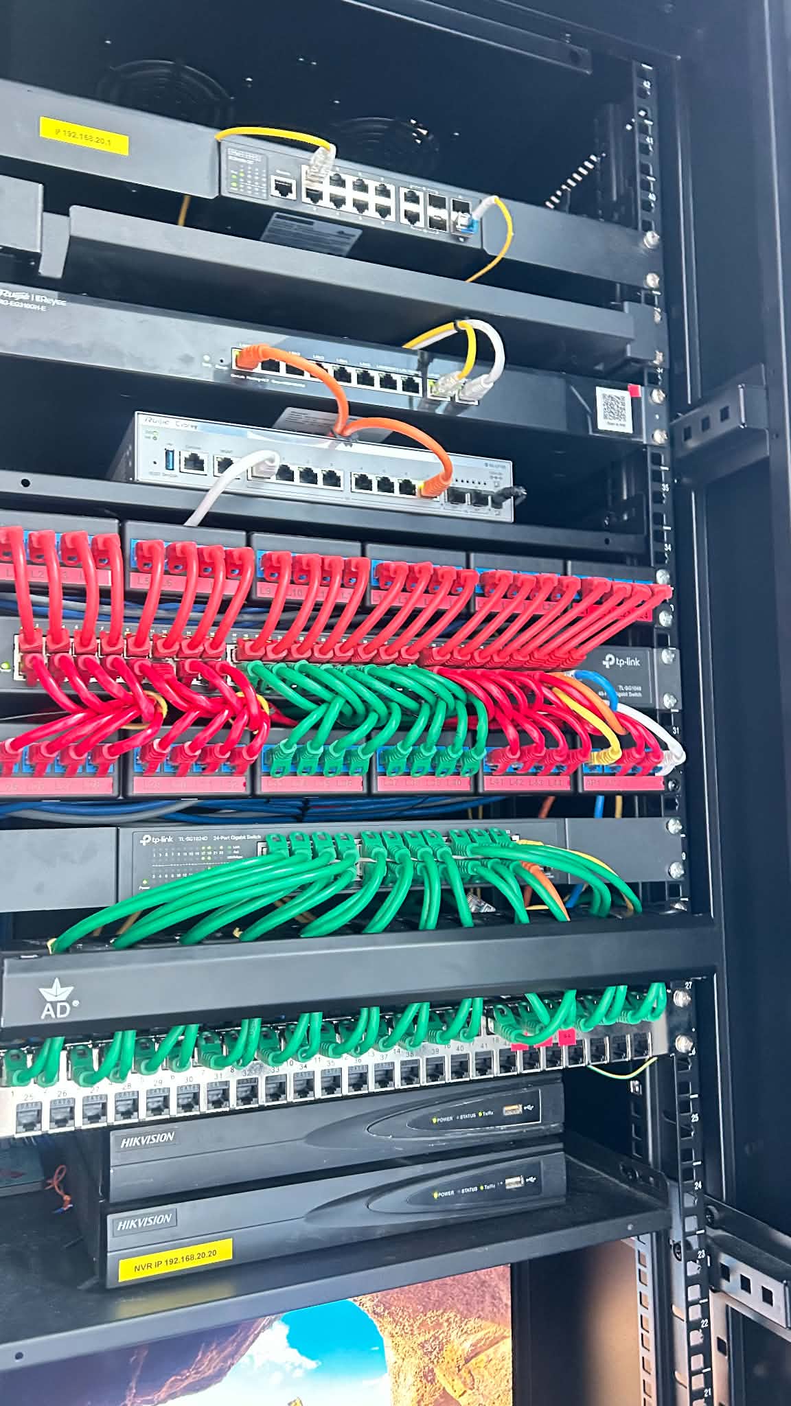 Close-up of rack-mounted switches and patch panels with neatly dressed red and green Cat6 patch cables above two Hikvision NVRs.