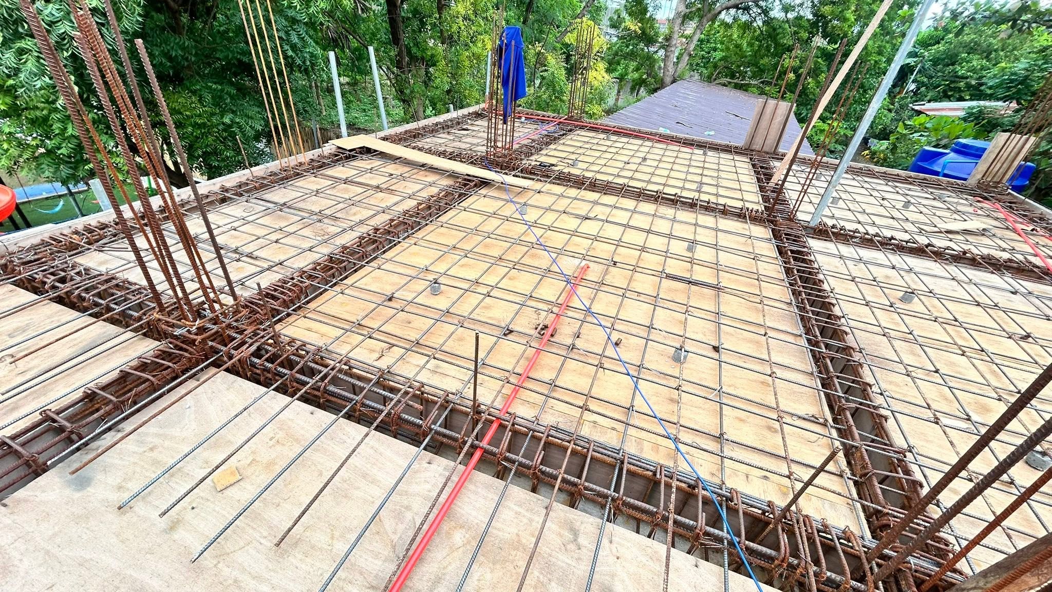 Red and blue conduit pipes routed diagonally across a wide steel rebar deck on a residential roof, ready for a concrete pour.