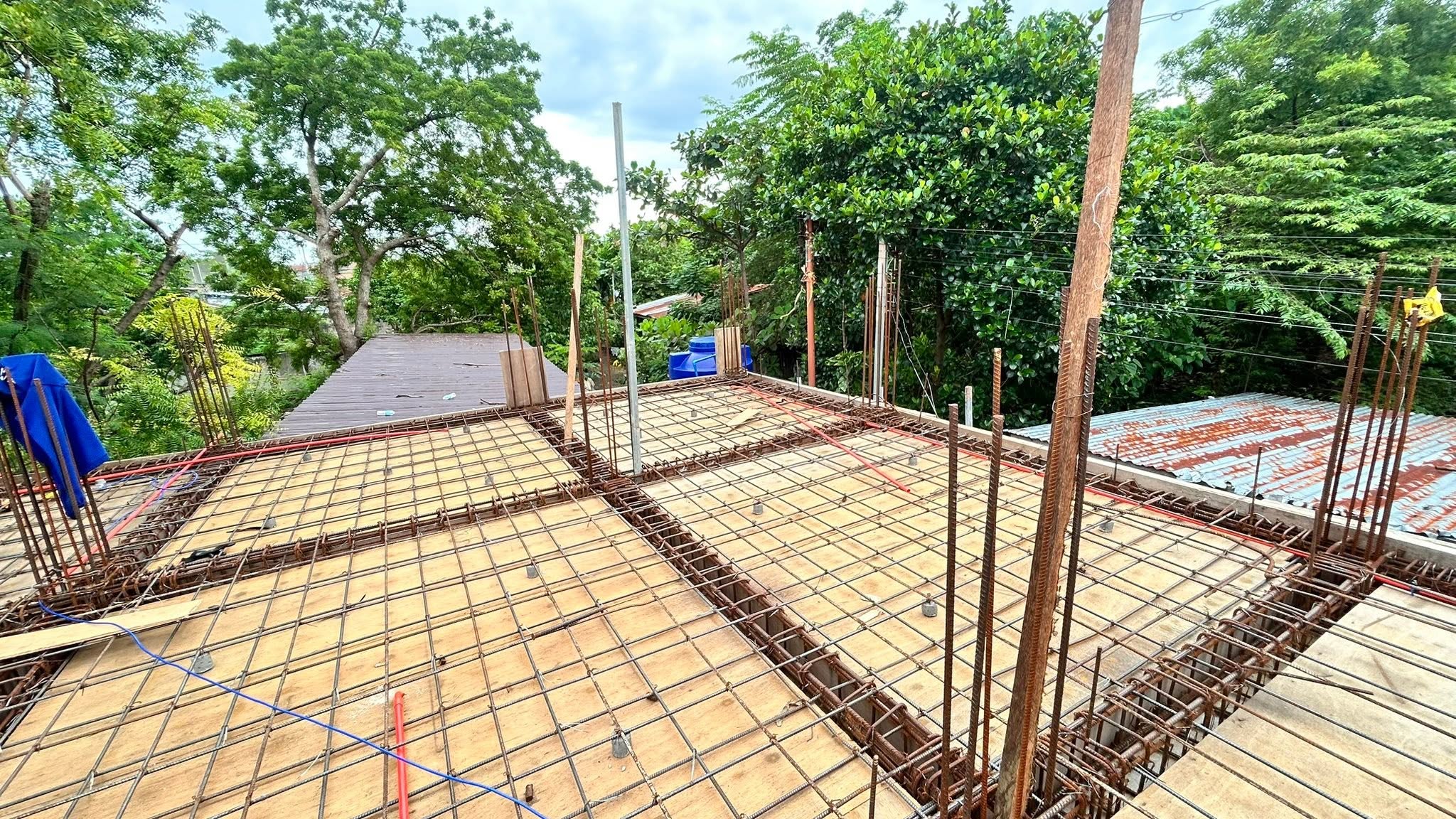A finished rebar deck with vertical dowel bars for the next floor, and a conduit line routed through the mesh, ready for the concrete pour.