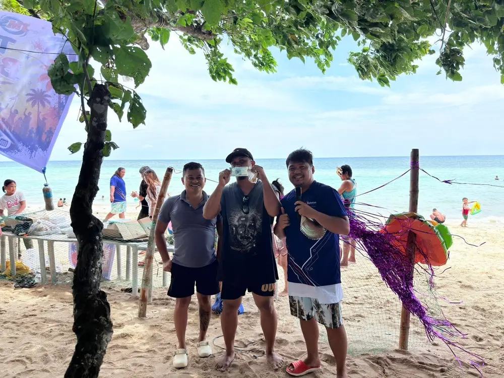 Three teammates posing together on the beach, one holding a seashell.