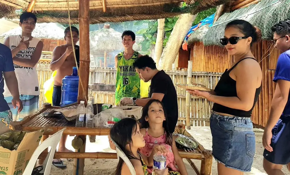 Teammates and their families sharing food together under a beach hut.