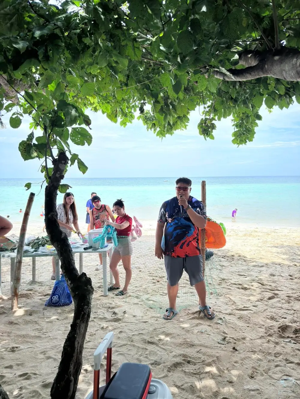A teammate singing on a microphone on the beach while others play with inflatable pool toys nearby.