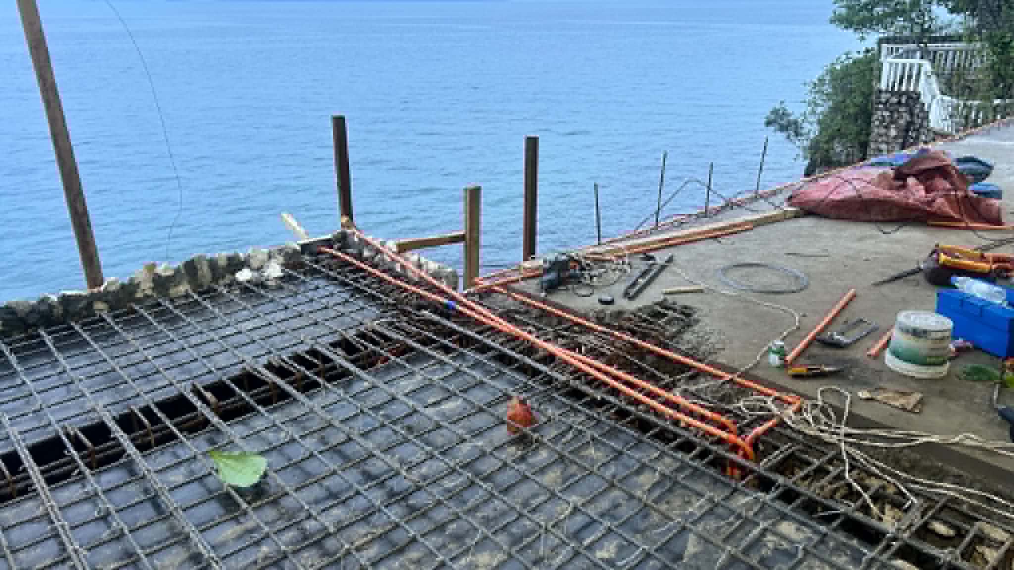 Steel rebar mesh deck under construction over the water at Turtle Point, Catmon, Cebu, with orange conduit pipes routed through the grid before the concrete pour.