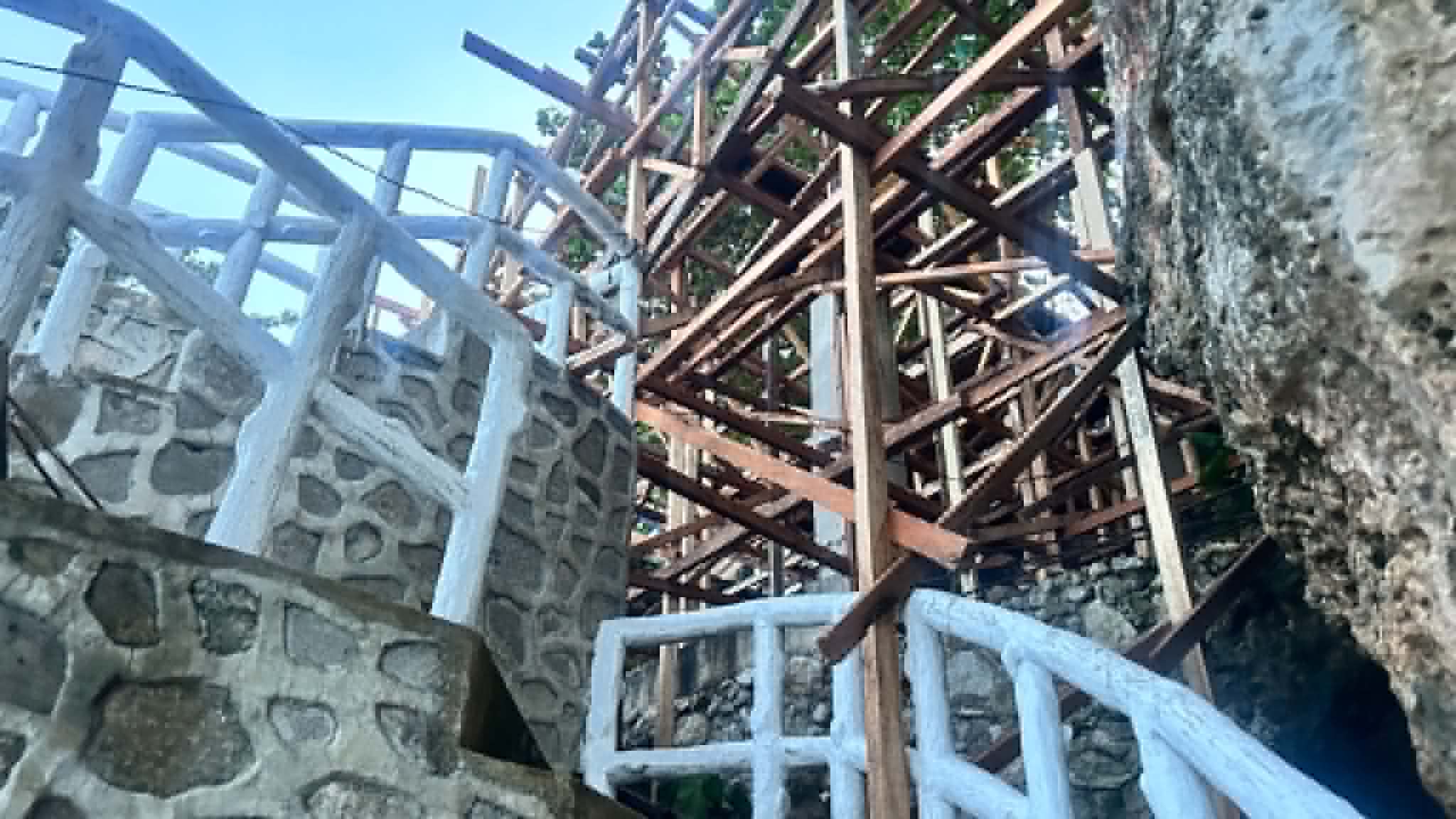 Wooden and steel scaffolding beside a stone masonry railing under construction on the cliffside at Turtle Point.